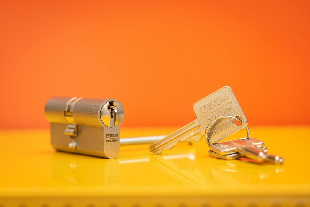 Schließzylinder von ASSA ABLOY, SK6 Sperrtechnik mit Schlüssel vor Orange- Gelben Hintergrund. Studioaufnahme.