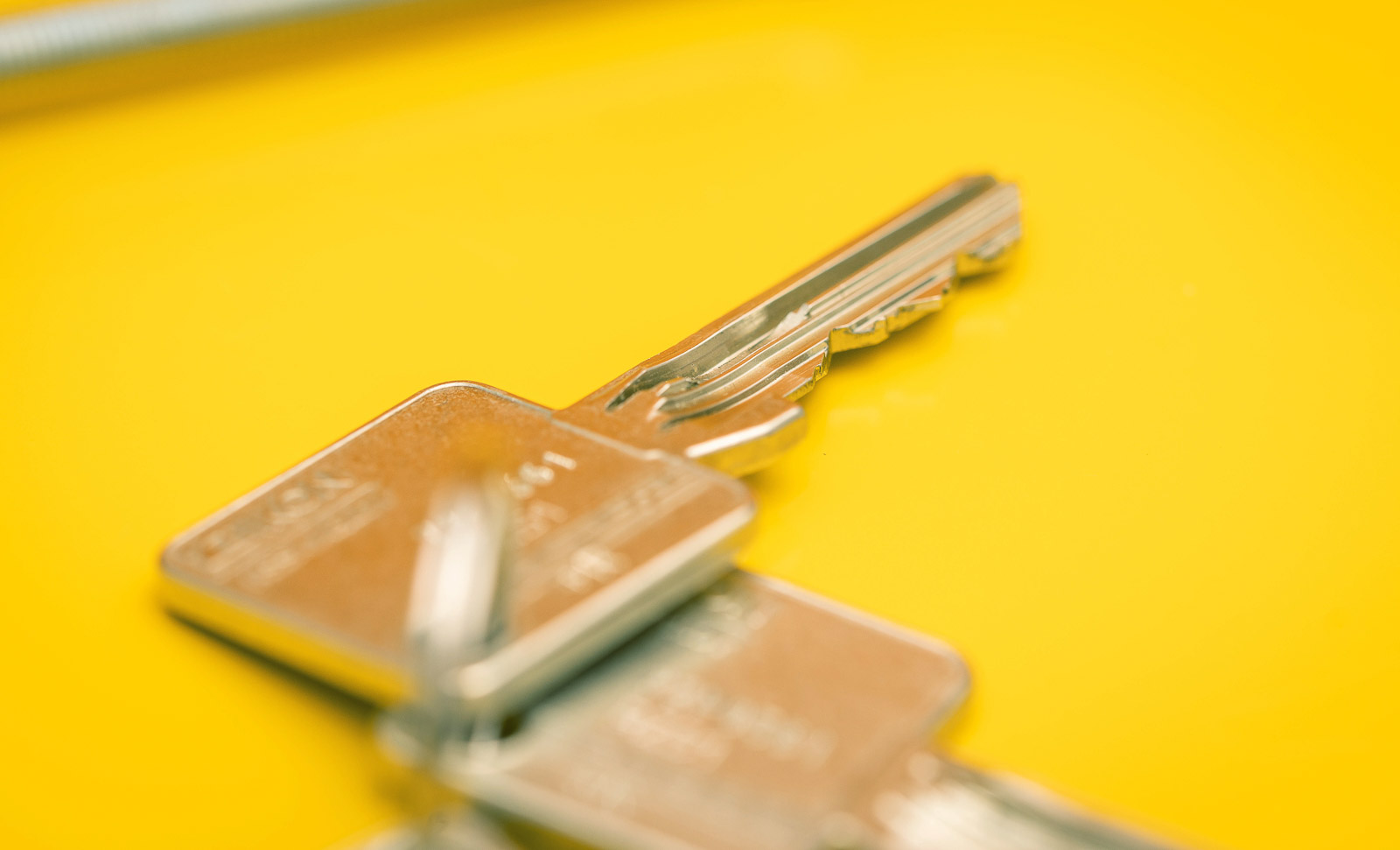 Schlüssel von ASSA ABLOY, SK6 Sperrtechnik im Detail vor Gelben Hintergrund. Studioaufnahme.