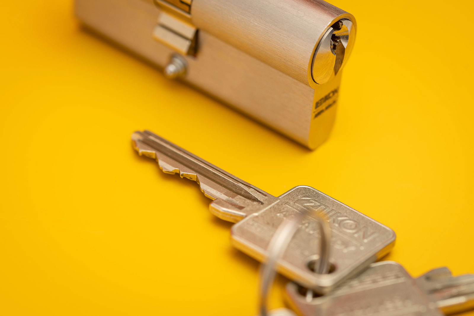 Schlüssel von ASSA ABLOY, SK6 Sperrtechnik im Detail vor Gelben Hintergrund. Studioaufnahme.