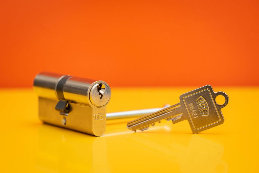 Schließzylinder BKS mit Schlüssel vor Orange- Gelben Hintergrund. Studioaufnahme.