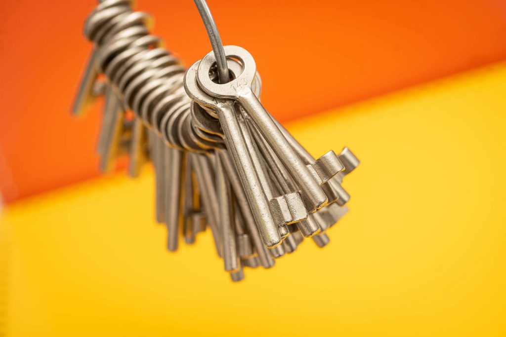 Verschiedene Buntbartschlüssel als Bund an einem Schlüsselring. Orange und Gelber Hintergrund.